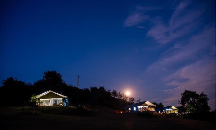 Three safari tents nestled into the hillside at night